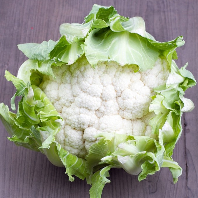 Fresh Igloo cauliflower head with green leaves on wooden surface