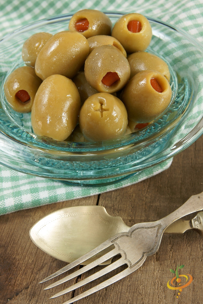 Bowl of green olives stuffed with sweet pimento peppers on a wooden table with vintage fork and spoon