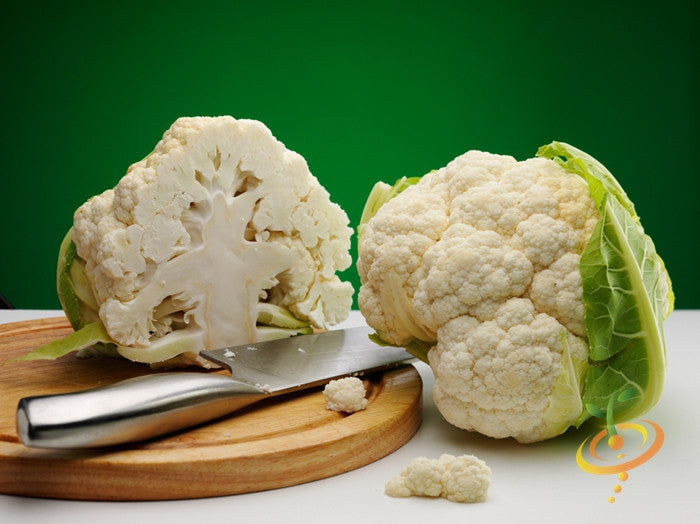 Fresh Igloo cauliflower heads with dense leaves on wooden cutting board and green background