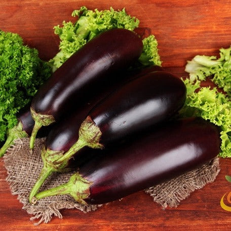 Three glossy dark purple eggplants on burlap surrounded by green lettuce leaves on wooden surface, representing Eggplant - Florida Market seeds.