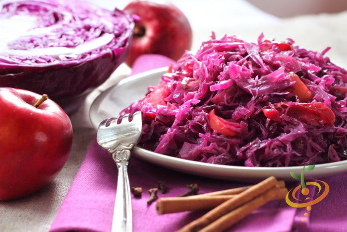 Plate of red cabbage salad made from Mammoth Red Rock cabbage with whole red cabbages and apples in the background