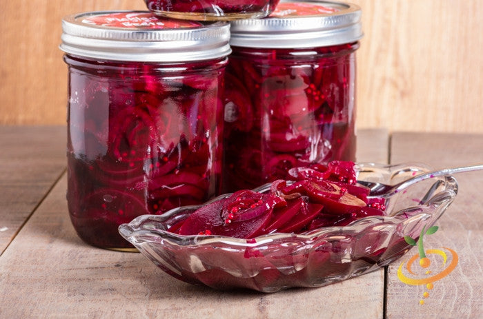 Jars of pickled Bulls Blood beets with sliced beets in a glass dish on wooden surface