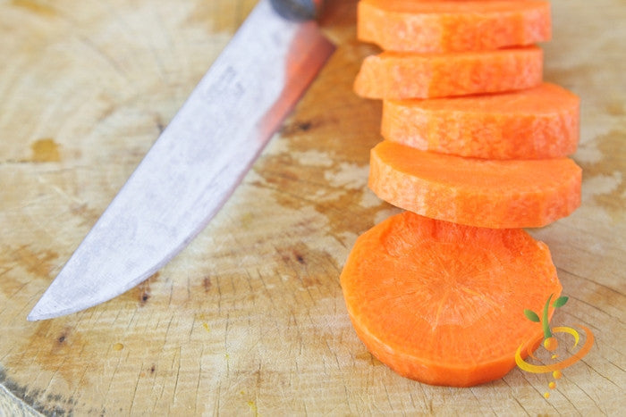 Sliced bright orange Chantenay carrot rounds on wooden cutting board with knife