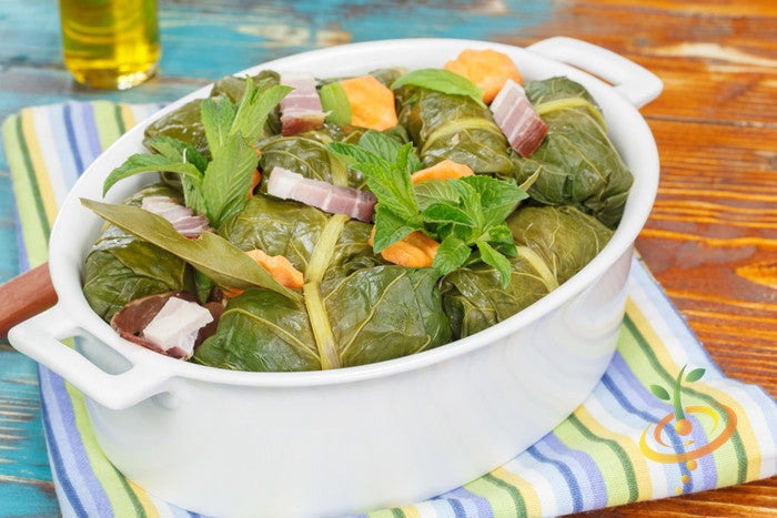White dish of collard green wraps with ham and vegetables on striped cloth on wooden table