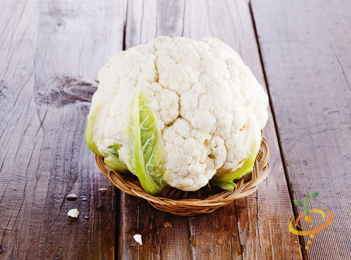 Fresh Igloo cauliflower head with green leaves in a wicker basket on wooden surface