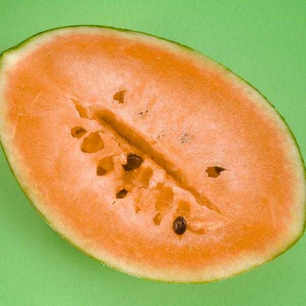 Close-up of a ripe watermelon with bright orange flesh and minimal seeds on a green background, representing Watermelon Tendersweet Orange-flesh seeds variety.